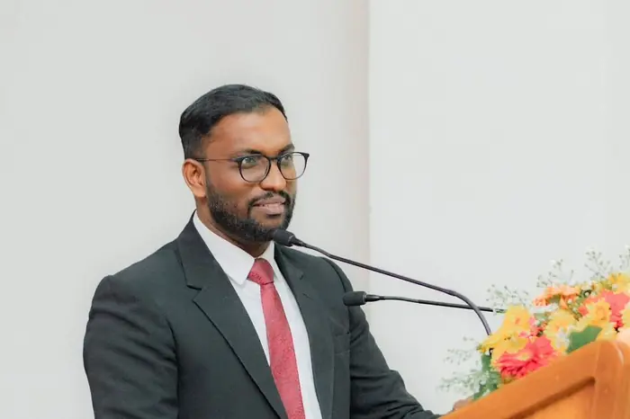 Mayantha in a black suit and red tie speaking at a podium for the Law Students' Association of Sri Lanka