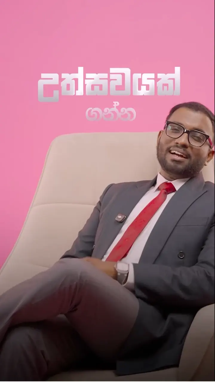 Mayantha presenting to camera in a dark suit against a pink set, for Invitation.lk