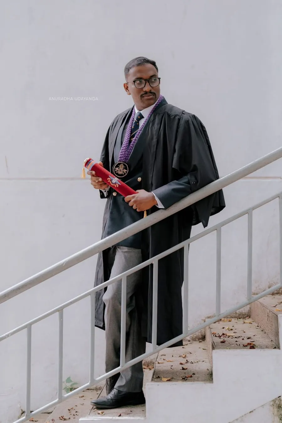 Mayantha in academic gown holding his degree scroll on the steps at graduation