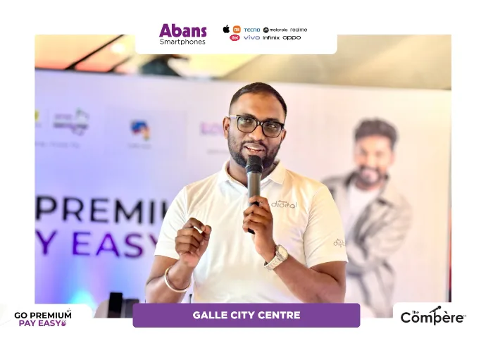 Mayantha Warnakulasooriya hosting and presenting on stage at the Abans Go Premium Pay Easy island-wide campaign launch event, holding a microphone in professional formal wear against branded promotional backdrops.