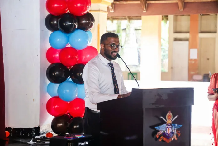 Mayantha Warnakulasooriya acting as the official compere on stage and interacting during the community aid distribution program organized by KDU, holding a microphone while guiding the event and engaging with attendees.