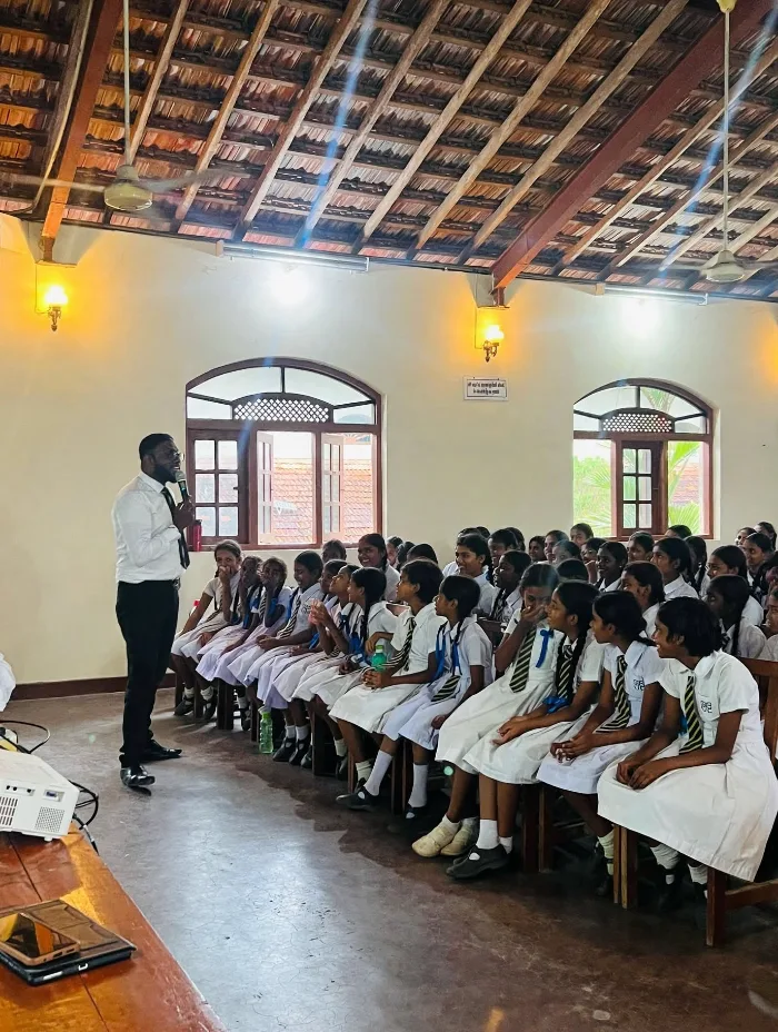 Uditha Mayantha speaking to an audience of school students in uniforms during an interactive School Legal Awareness Program in Sri Lanka.